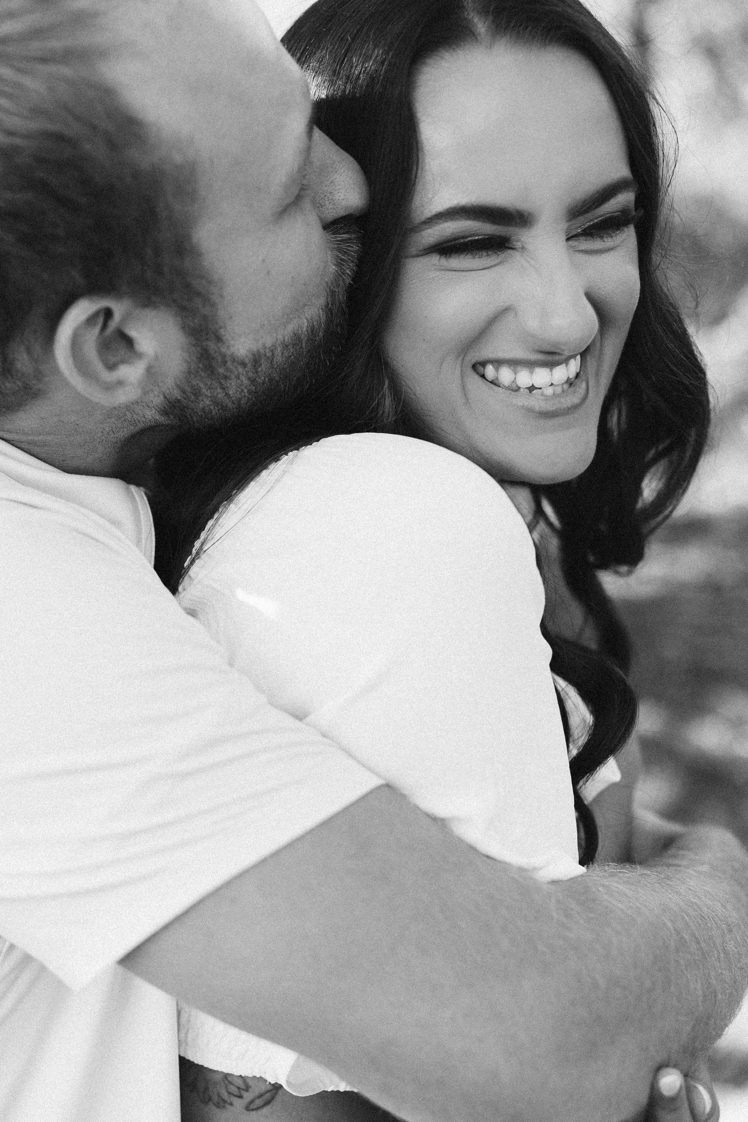 Black and white portrait of a joyful couple sharing an intimate moment outdoors.