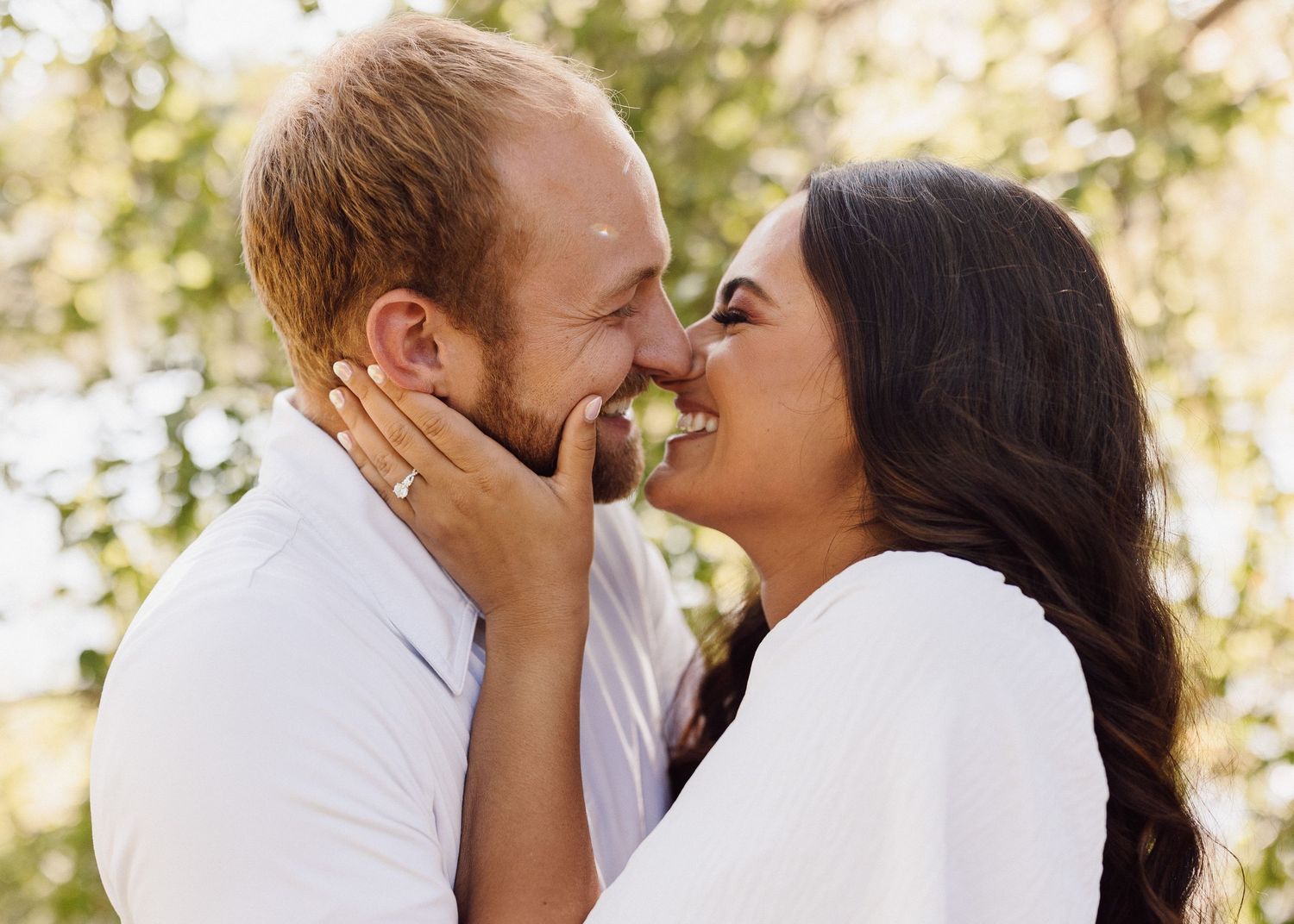 Loving couple in white sharing a tender moment while touching foreheads and smiling.