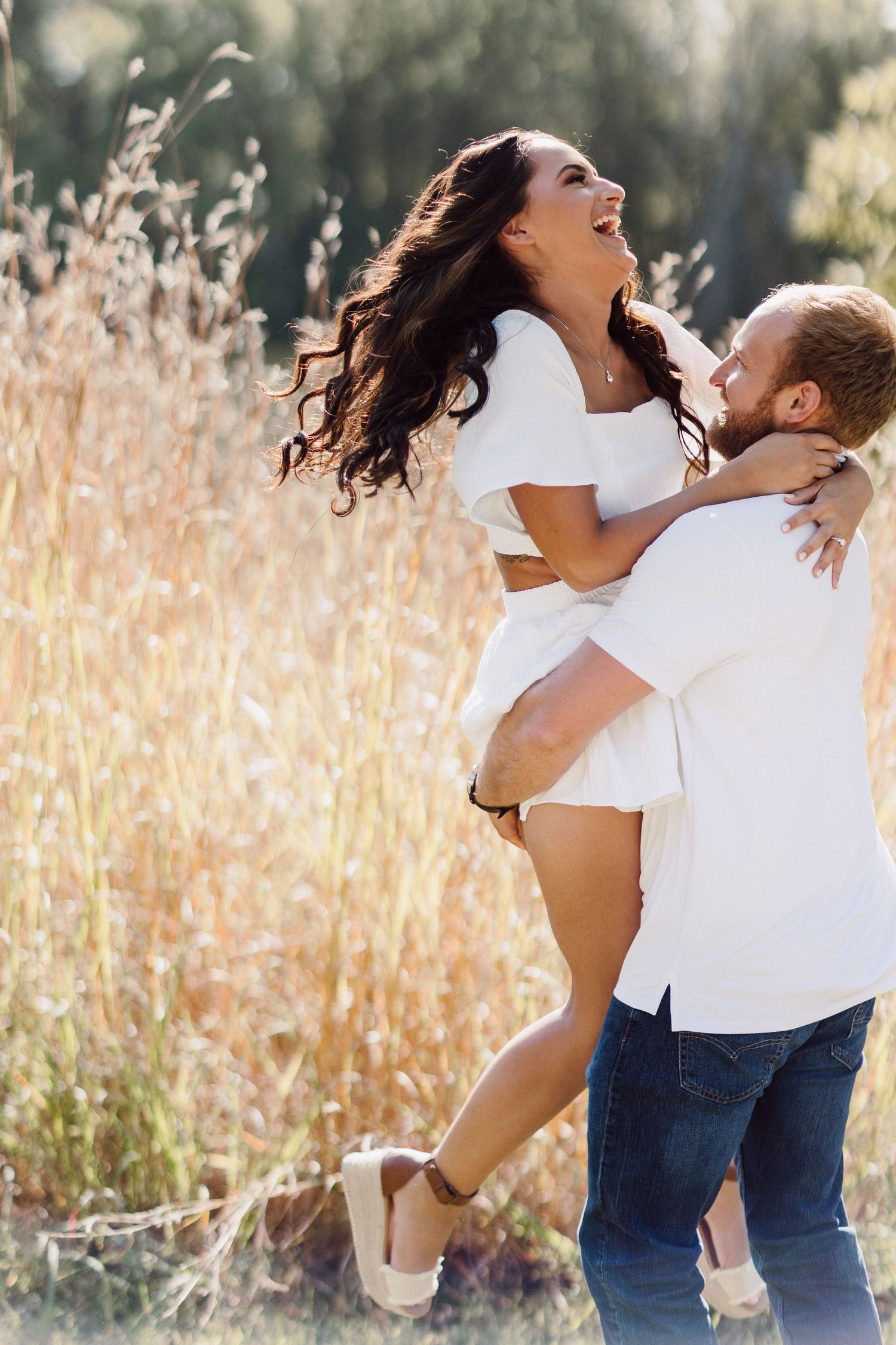 Joyful couple laughing and embracing in a sunlit field of tall golden grass.