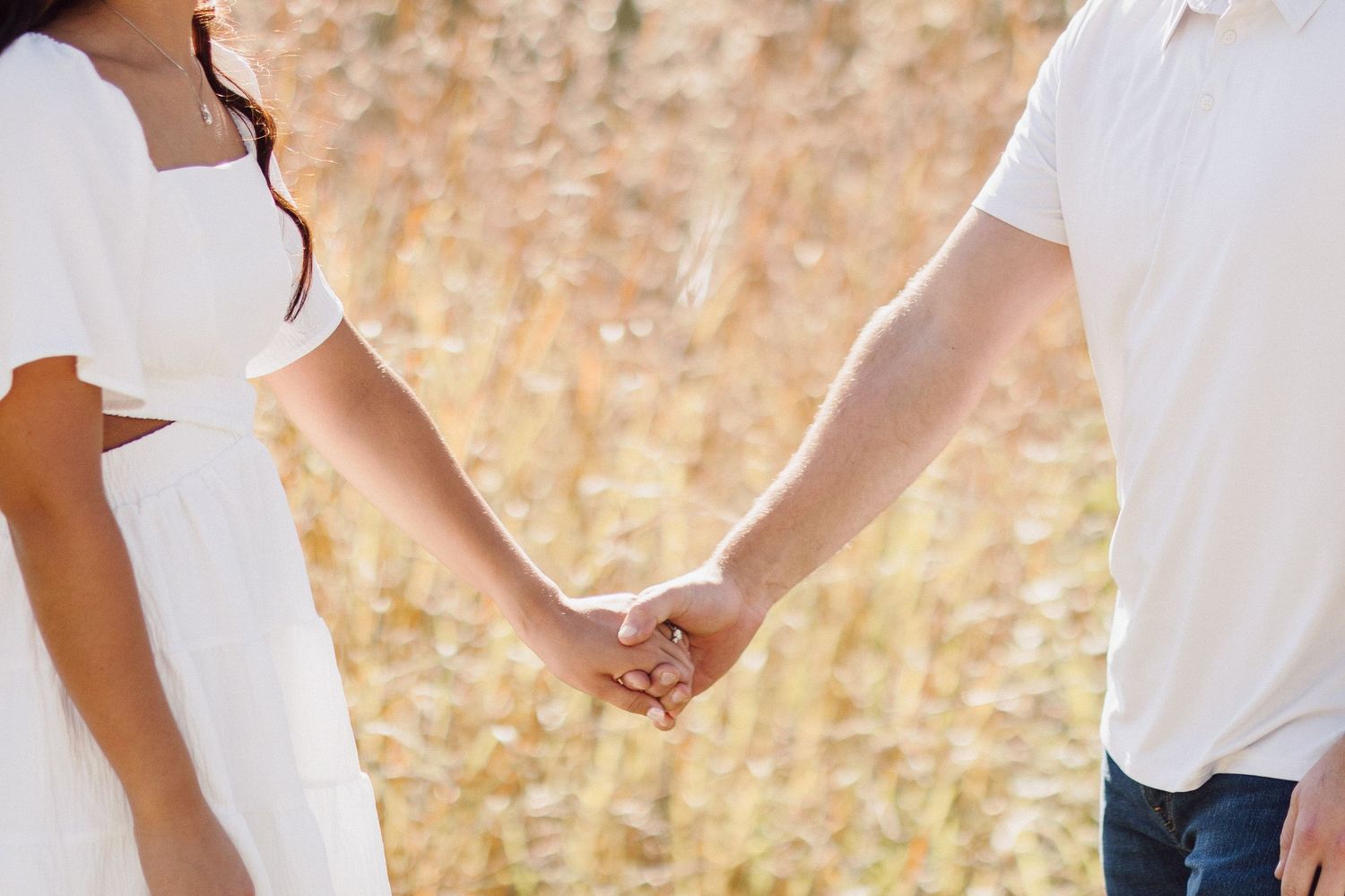 Close up of couple holding hands in a golden wheat field wearing white clothing.