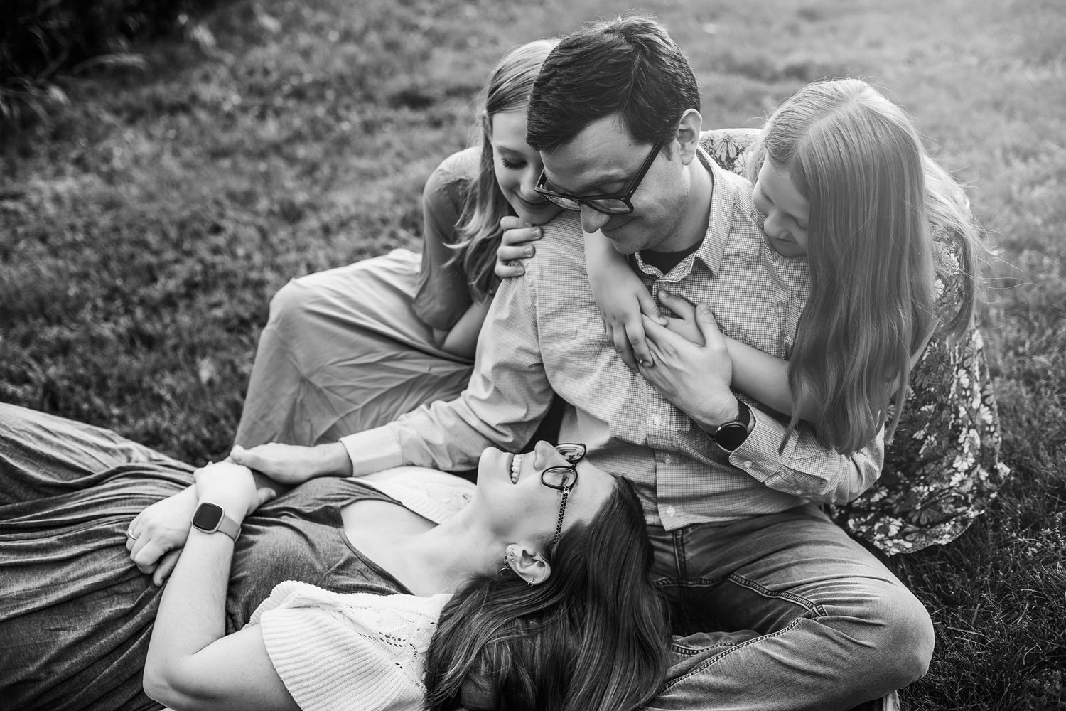 Black and white photo of a family laying in the grass together sharing an intimate moment outdoors.