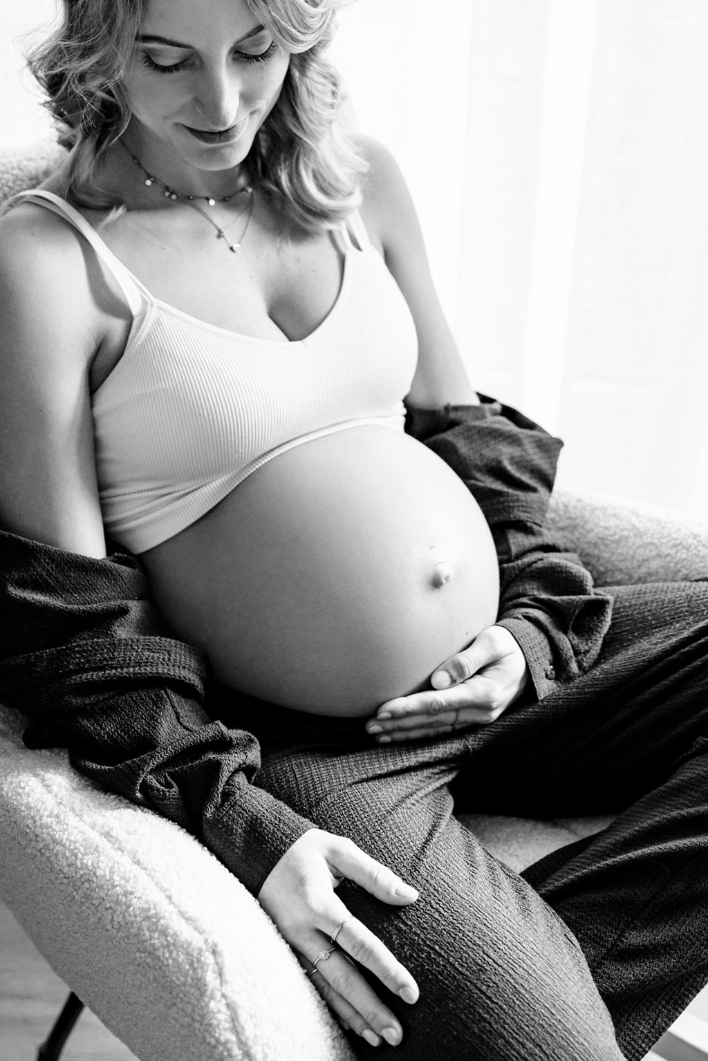 Zwart wit portret van een zwangere vrouw tijdens een lifestyle zwangerschapsshoot zittend in de schommelstoel bij het raam