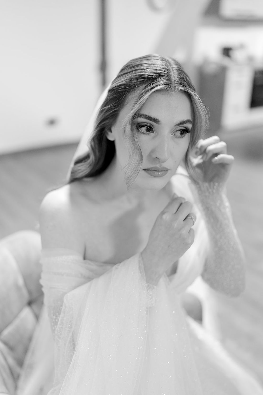 A black and white portrait of someone in an elegant off-shoulder wedding gown with soft, flowing fabric.