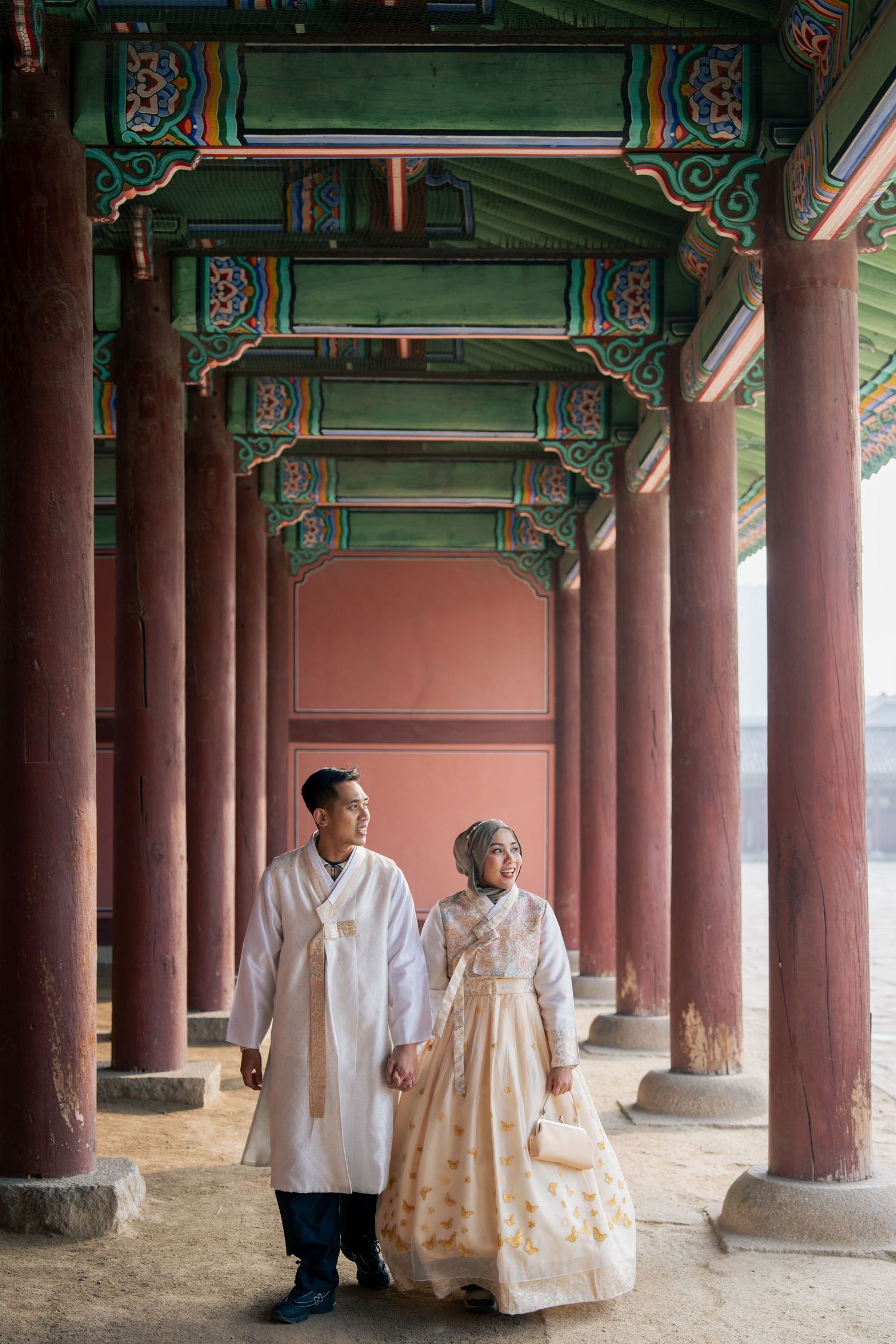 Traditional Korean hanbok-clad figures stand beneath ornate wooden pillars at a historic temple courtyard.