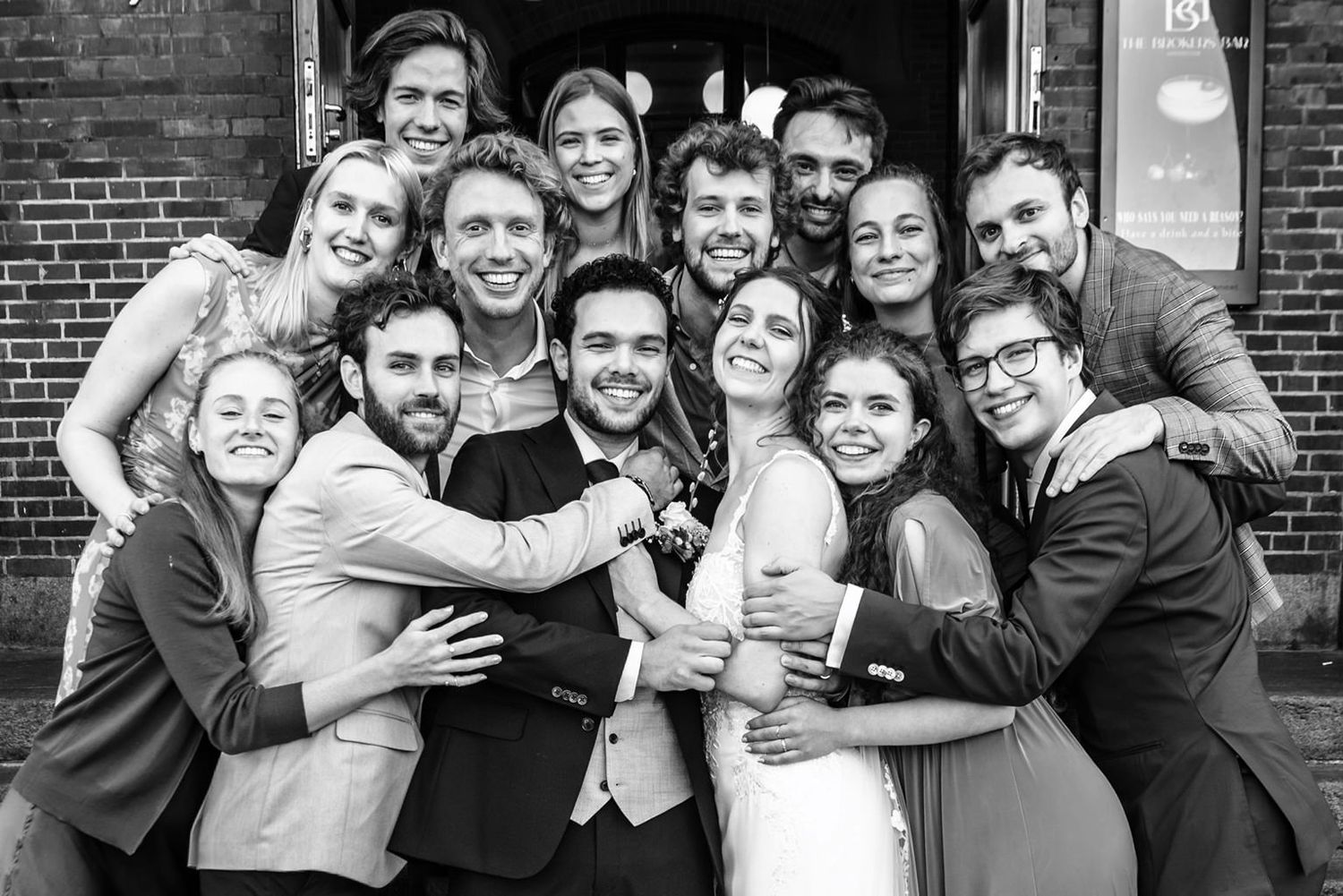 Groepsfoto van vrienden van Sharon en Quinten op het bordes van Meet Berlage, lachend en vrolijk, met het bruidspaar in het midden.