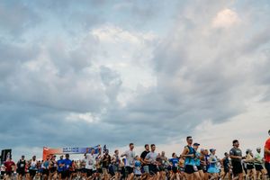 Large crowd of marathon runners gathered at a beach race event under cloudy skies.