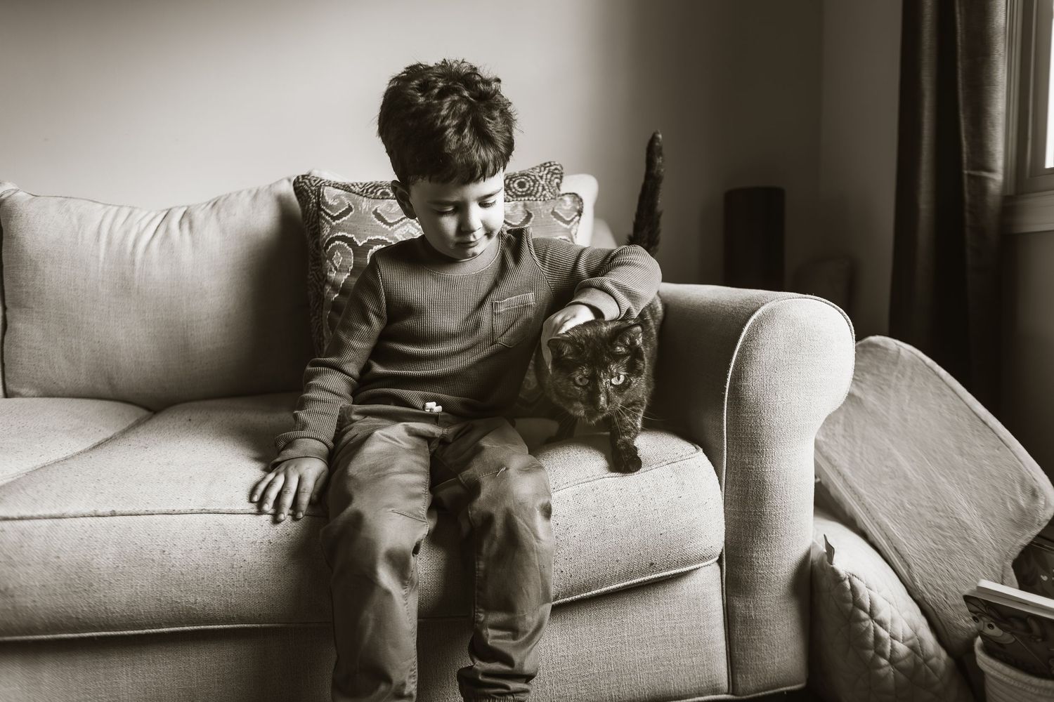 A playful cat and child interact together on a comfortable couch in a series of black and white photographs.