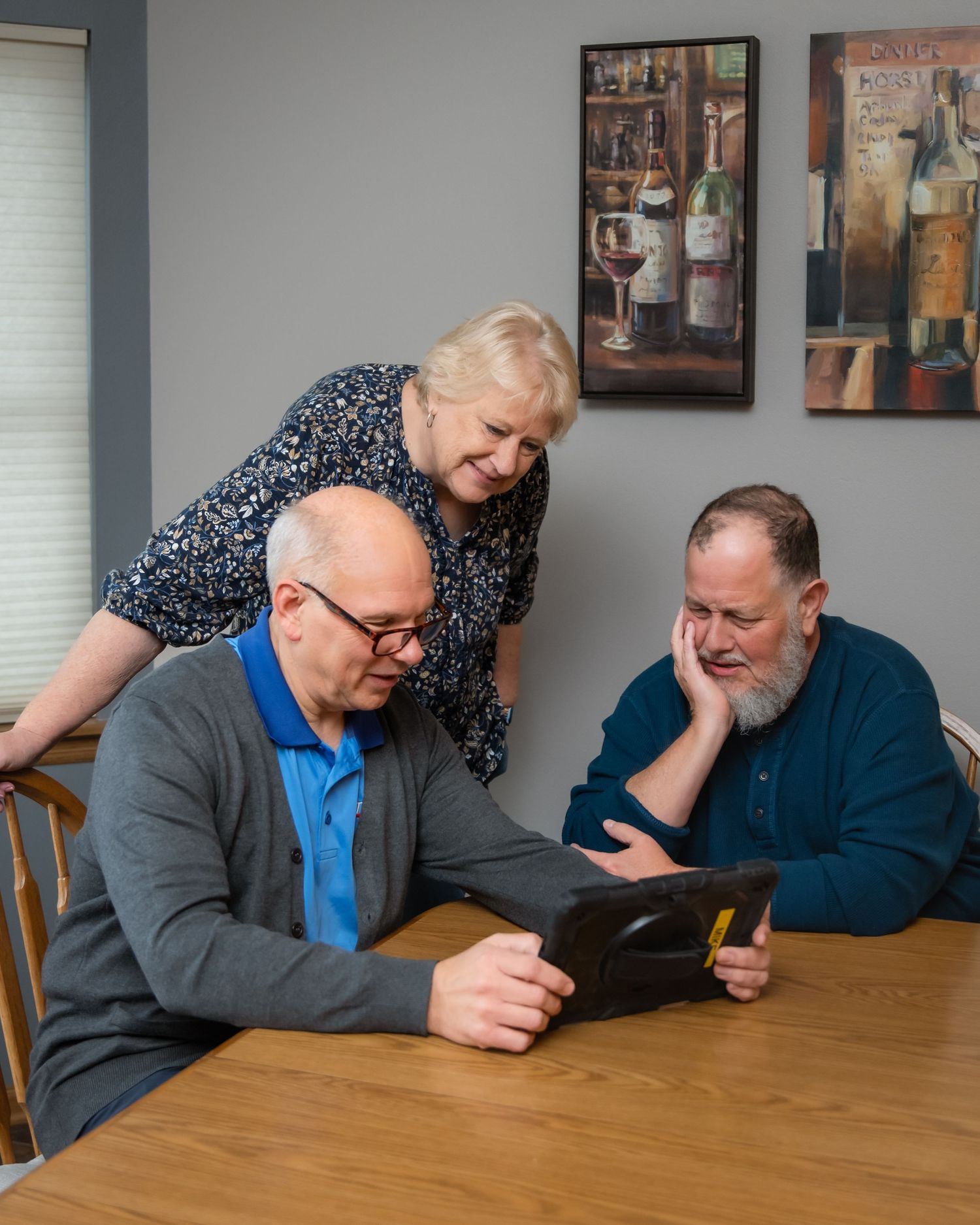 Three people sitting at a wooden table share a laugh while looking at their mobile phones.