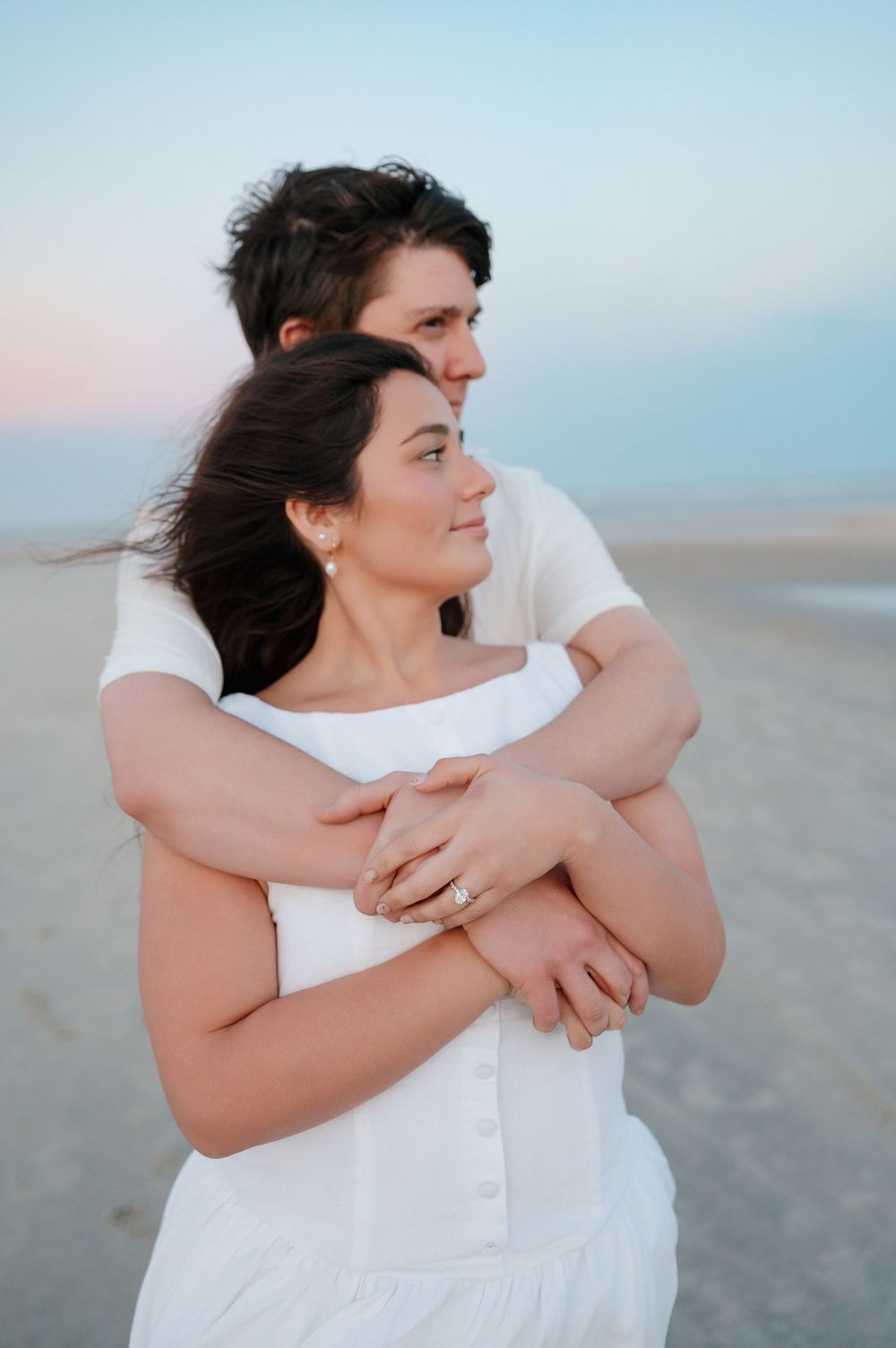 Intimate beach portraits capture tender moments between couple in white against soft sky.