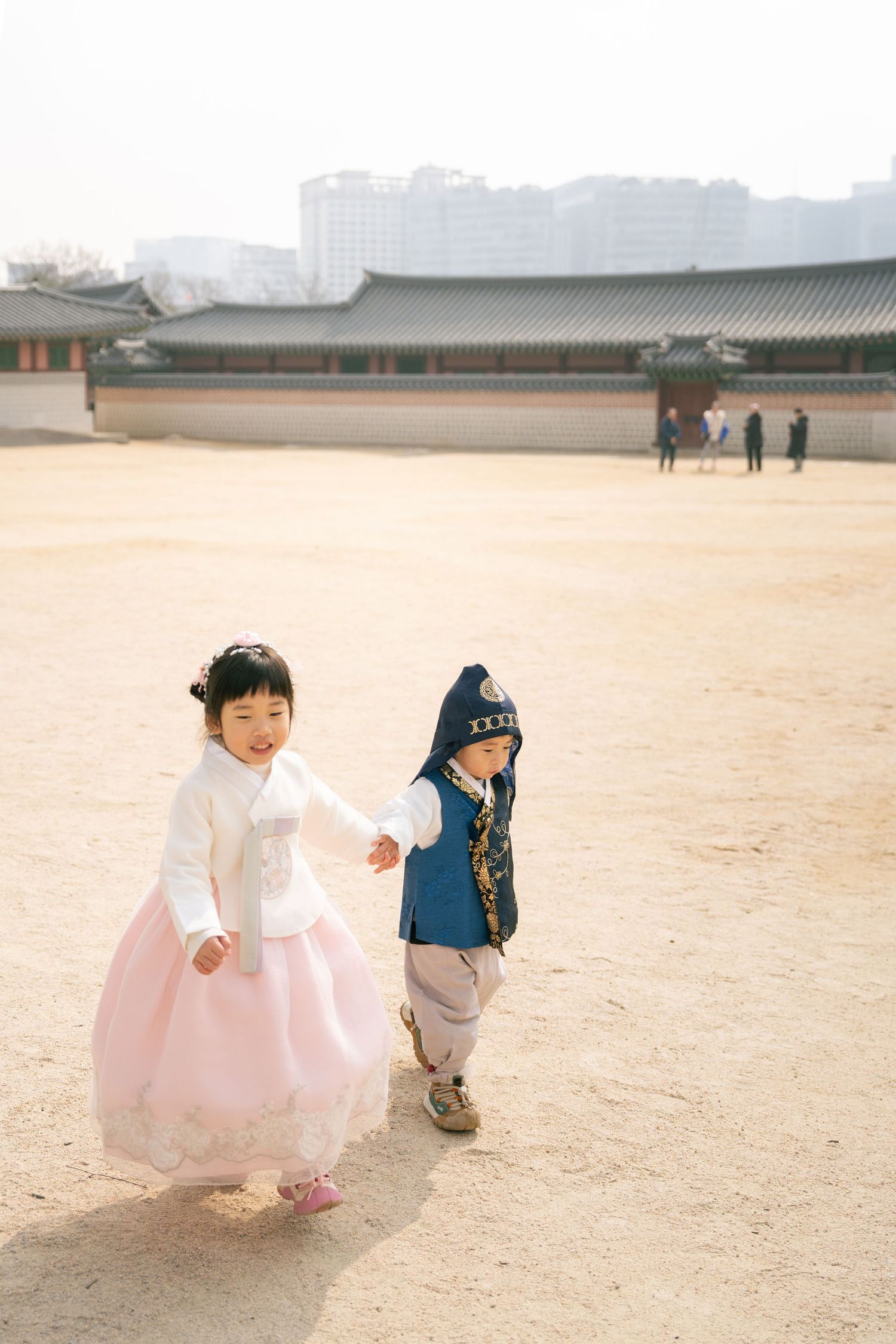 Two children play together in traditional Korean hanbok dress at a historic palace courtyard.
