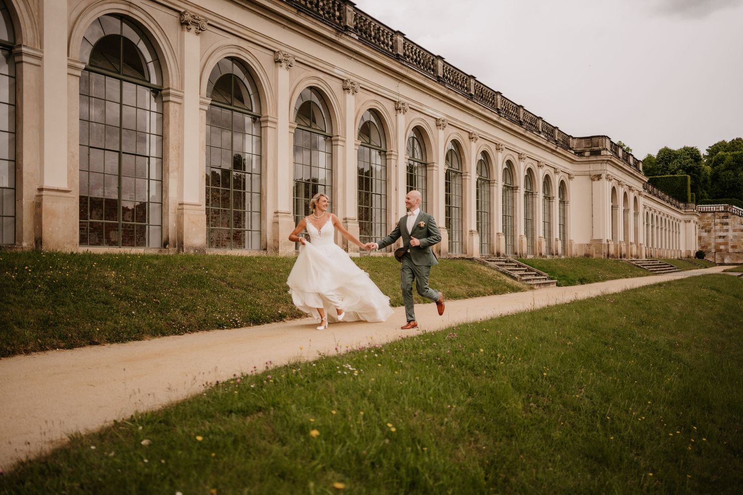A couple poses together on a stone pathway beside a historic building with arched windows and columns.