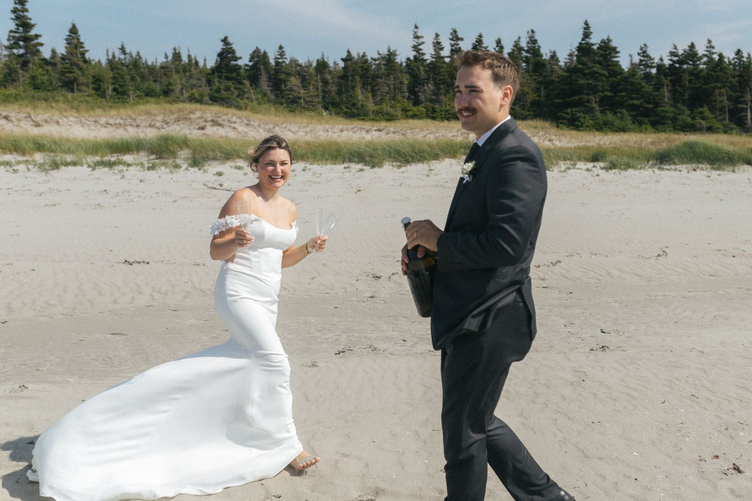 bride and groom laugh as they pop champagne on the beach in Tofino