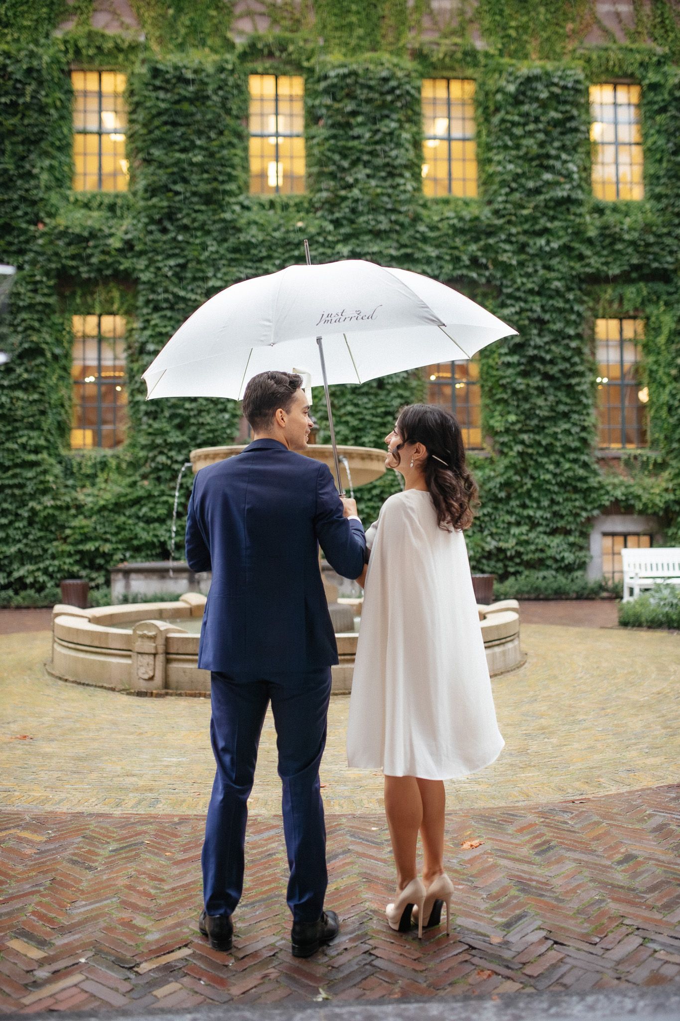 Bride and groom sharing an umbrella with the words "just married" on it in the courtyard or Stadhuis Rotterdam after their city hall wedding