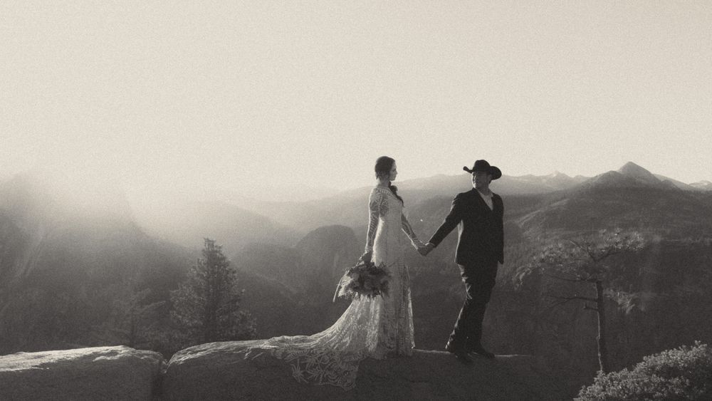 A couple in wedding attire stands silhouetted against a misty mountain landscape at sunset.