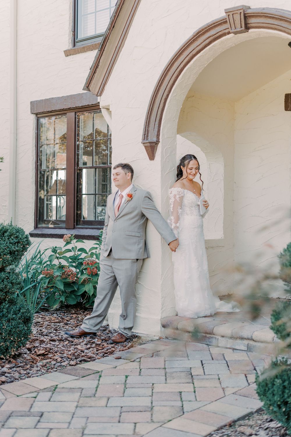 Bride and groom holding hands against a white arched building entrance on their wedding day.