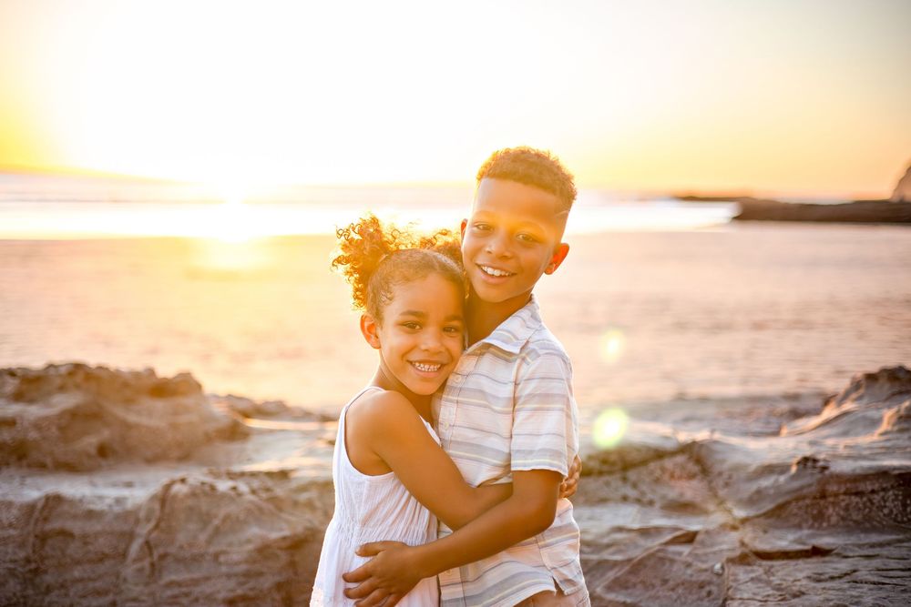 A couple embraces on rocky beach cliffs during golden hour sunset in Hawaii.