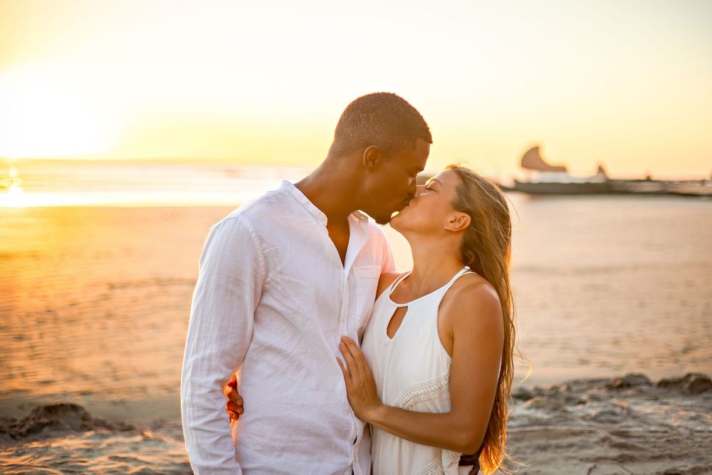 A couple shares a romantic moment on the beach at sunset with golden light illuminating the scene.