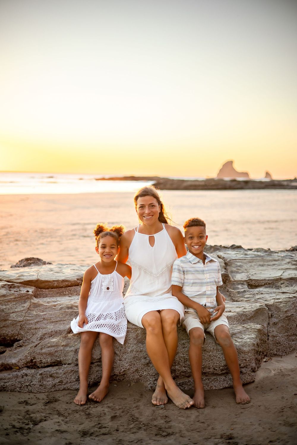A family sits together on coastal rocks during golden hour sunset at the beach.