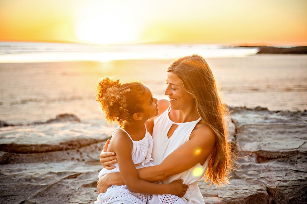 Couple embracing on beach during golden sunset with waves crashing behind them.