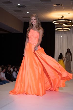 Flowing coral ballgown with sweetheart neckline displayed during evening wear segment.