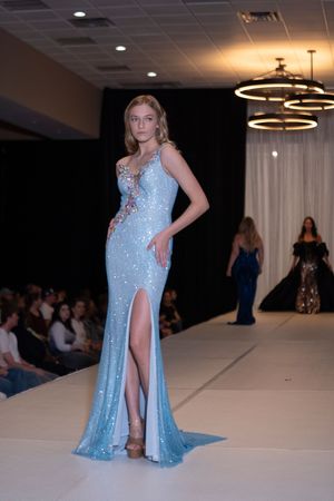 Model showcases sparkly light blue evening gown with high slit on fashion runway.