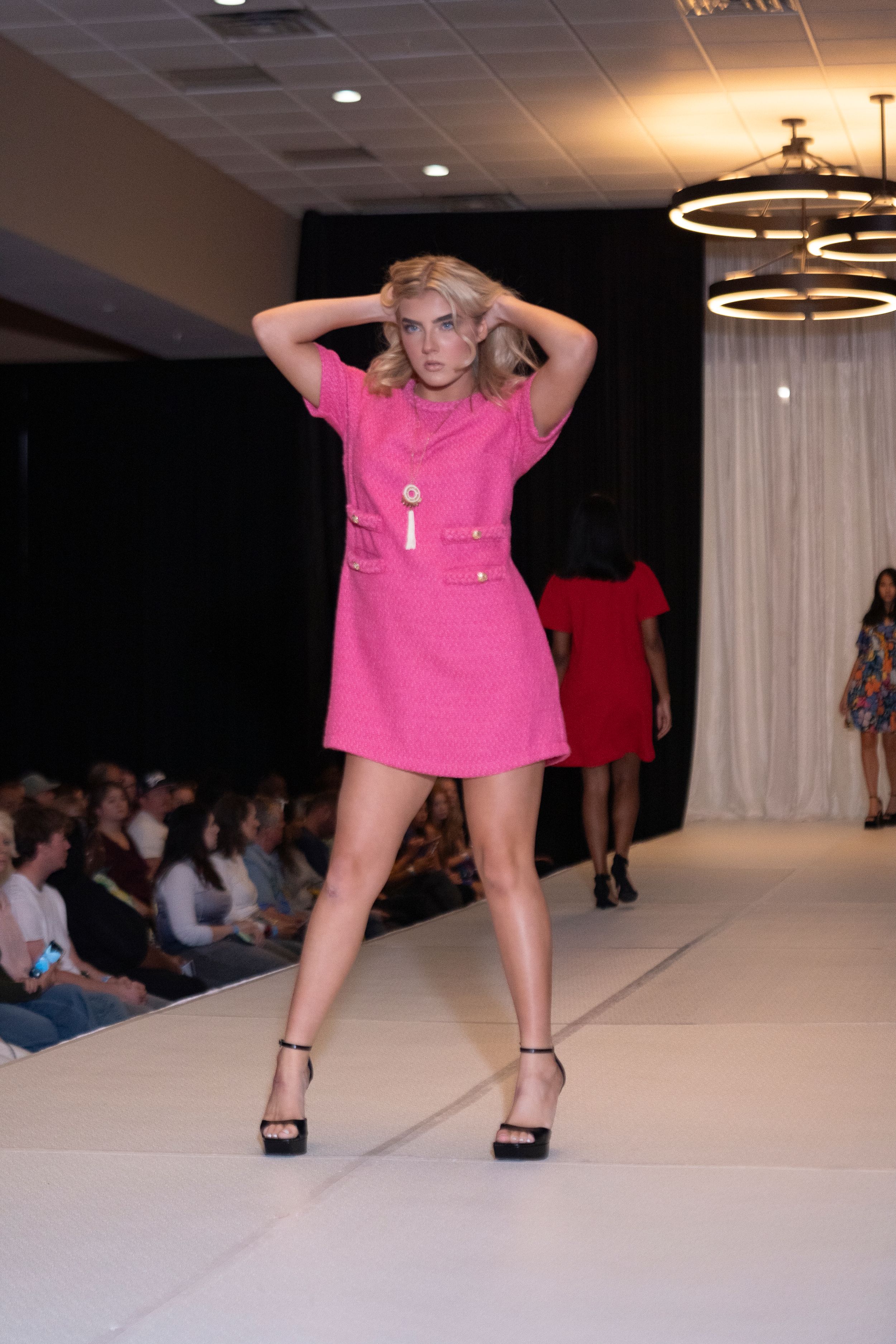 Model walks runway in bright pink t-shirt during fashion show.