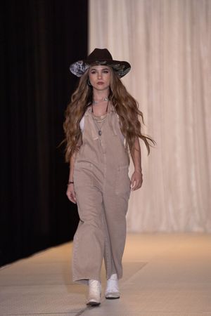 Model showcases beige overalls outfit on catwalk during fashion show presentation.