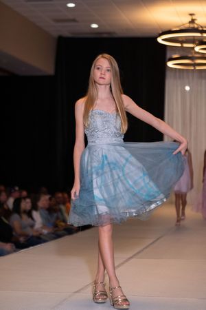 Model twirls in light blue tulle cocktail dress on fashion runway.