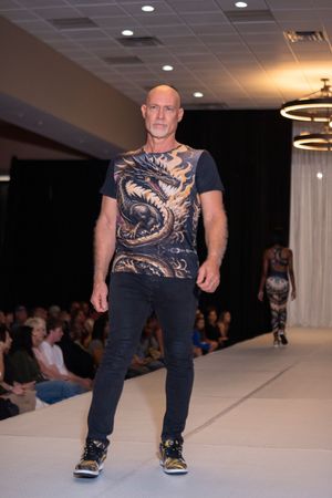 Fashion show models display coordinated dark athletic wear with copper-toned graphic designs on a lit catwalk.