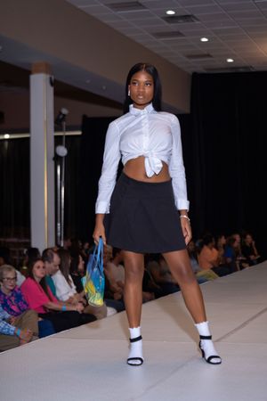 Fashion models present crisp white button-down shirts paired with black skirts on an illuminated runway.
