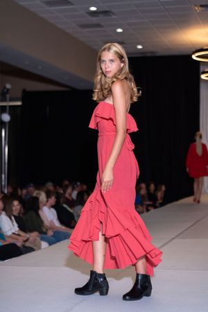 Coral ruffled dress paired with black ankle boots shown on fashion runway.