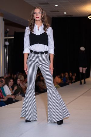 Models present retro-inspired outfits featuring striped bell-bottom pants and white blouses on the catwalk.