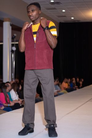 Model showcases burgundy and gray colorblock outfit on white runway during fashion event.