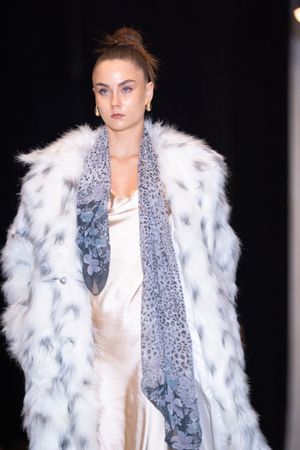 Luxurious white fur coat paired with grey scarf and cream dress on fashion catwalk.