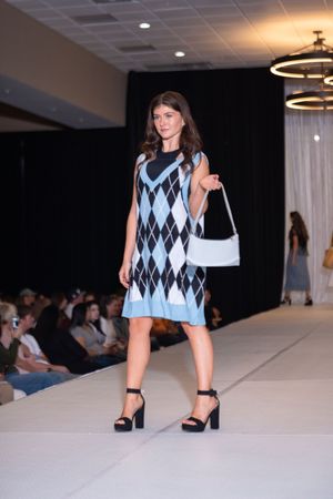 Model walks runway in blue and white argyle pattern dress with black heels.