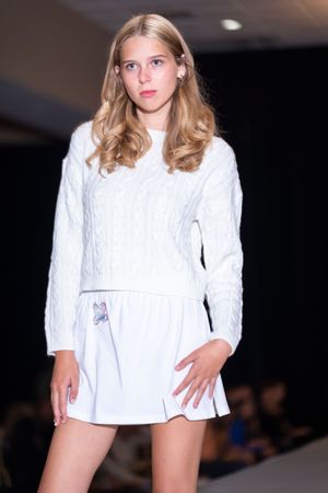 Model in white cable knit sweater dress poses dynamically on fashion runway.