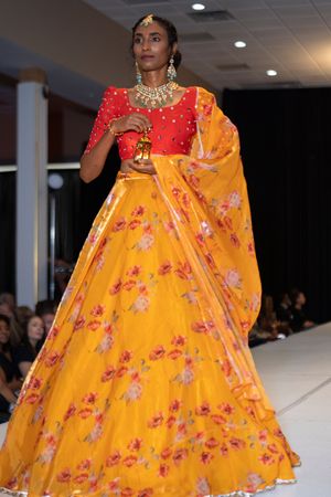 Traditional Indian lehenga in vibrant yellow and red with intricate floral patterns on fashion runway.