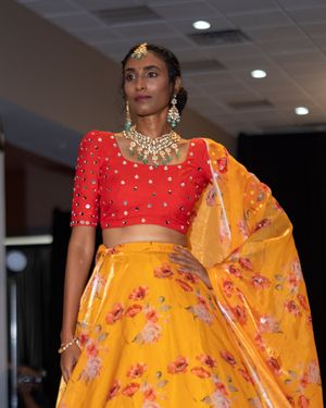 Traditional Indian fashion ensemble featuring a bright red crop top and yellow floral dupatta displayed in an indoor setting.