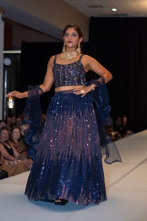 A sparkling navy blue lehenga with sequins and traditional jewelry being showcased on a fashion runway.