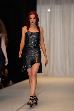 Sleek cocktail dress in iridescent black material with asymmetric hem on catwalk.