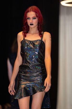 A shimmering black mini dress with iridescent details displayed on a fashion catwalk.