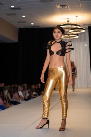 Models walk runway in black lace tops and metallic gold pants during fashion show event.