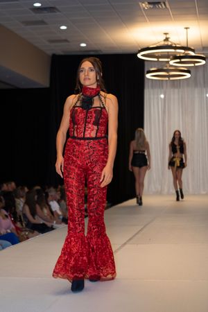 Models walk the runway showcasing elegant red and black formal wear at a fashion show event.