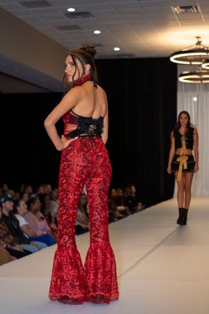 Red velvet bell-bottom pants with a black top shown from behind on a fashion runway.