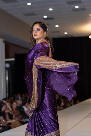 Model displays purple and gold embellished traditional South Asian outfit with flowing fabric on runway.