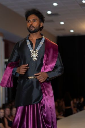 A luxurious black and purple velvet ensemble with ornate jewelry displayed at a fashion show.