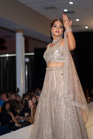 Sparkling silver lehenga with intricate embellishments and sheer cape showcased on fashion runway.