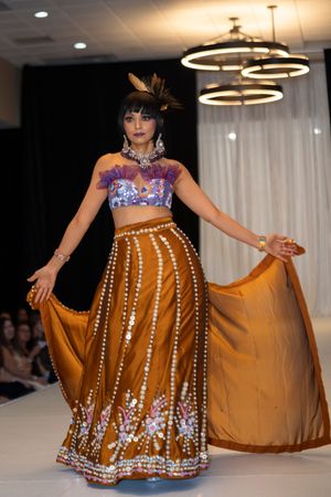 Fashion model showcases ornate brown lehenga with pearl embellishments and floral details on runway.