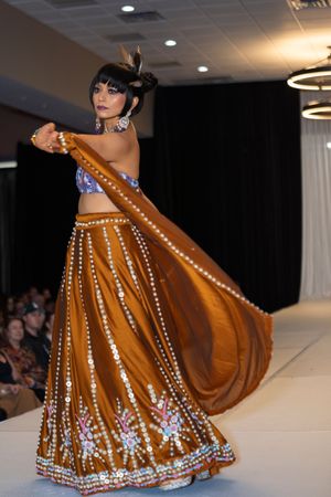 A traditional brown and gold embellished lehenga being twirled on the runway.
