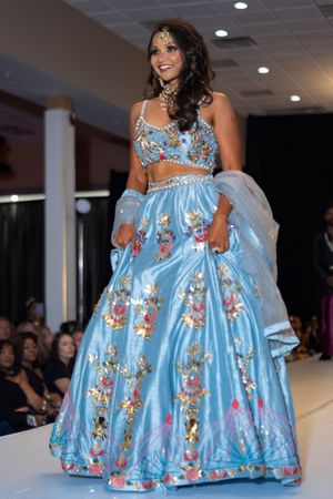 A light blue two-piece gown with floral details and sheer fabric being showcased at a fashion event.